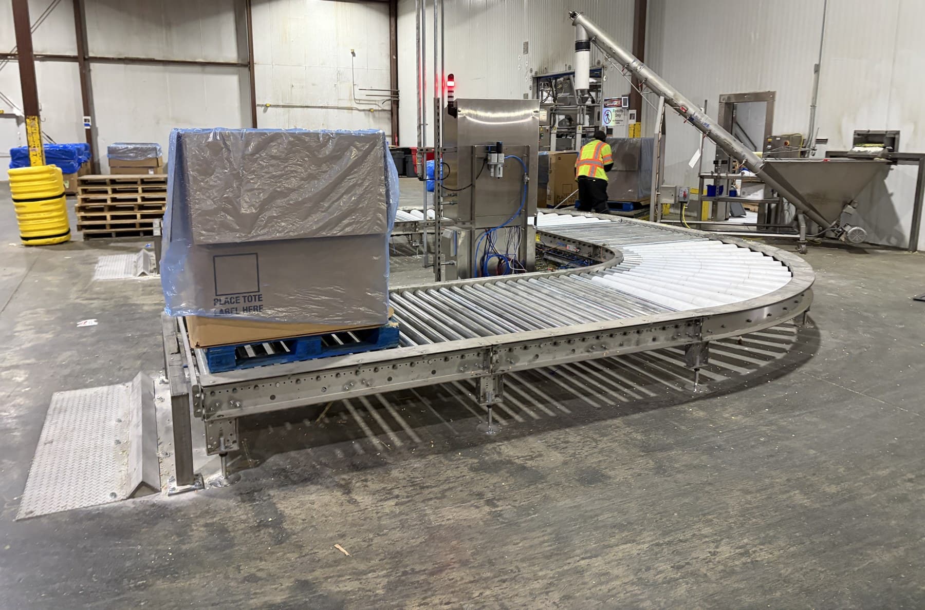 A blue pooled rental pallet with a lined tote staged at the infeed of a stainless 24 VDC MDR pallet circuit in a processing plant