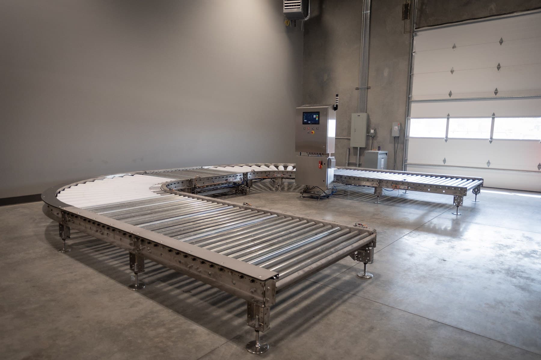 Stainless 24 VDC MDR pallet conveyor circuit with swept-radius corners and a scale deck, on the AQS shop floor