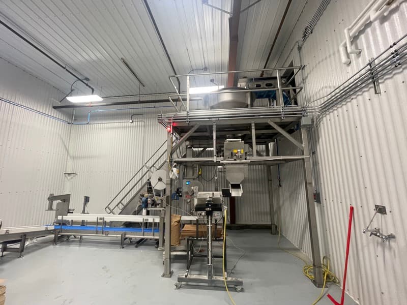 Elevated stainless incline conveyor feeding a mezzanine in a food production facility