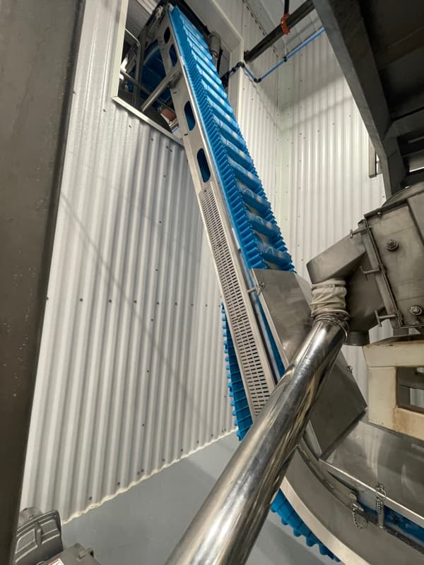 Stainless steel incline conveyor with cleated belt for positive product control at elevation changes