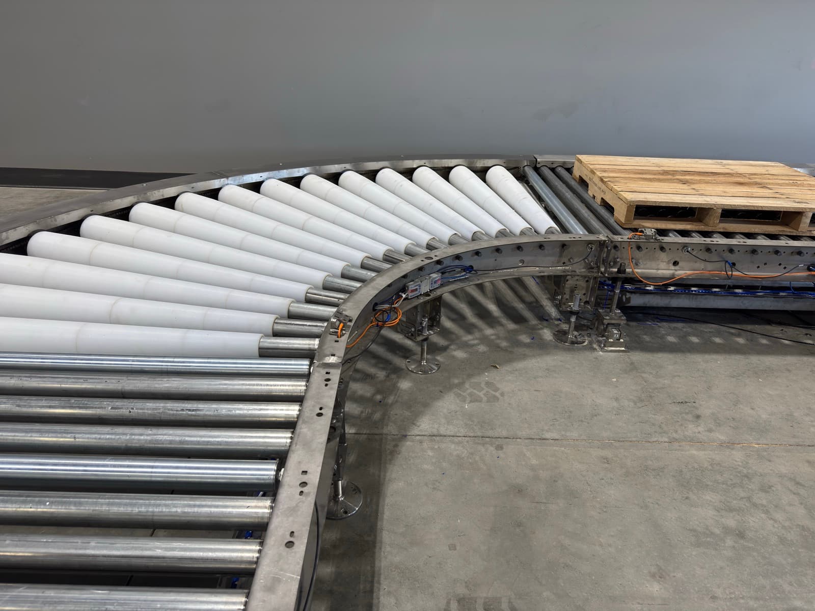 Loaded pallet riding the white tapered rollers of a stainless 24V MDR pallet conveyor curve