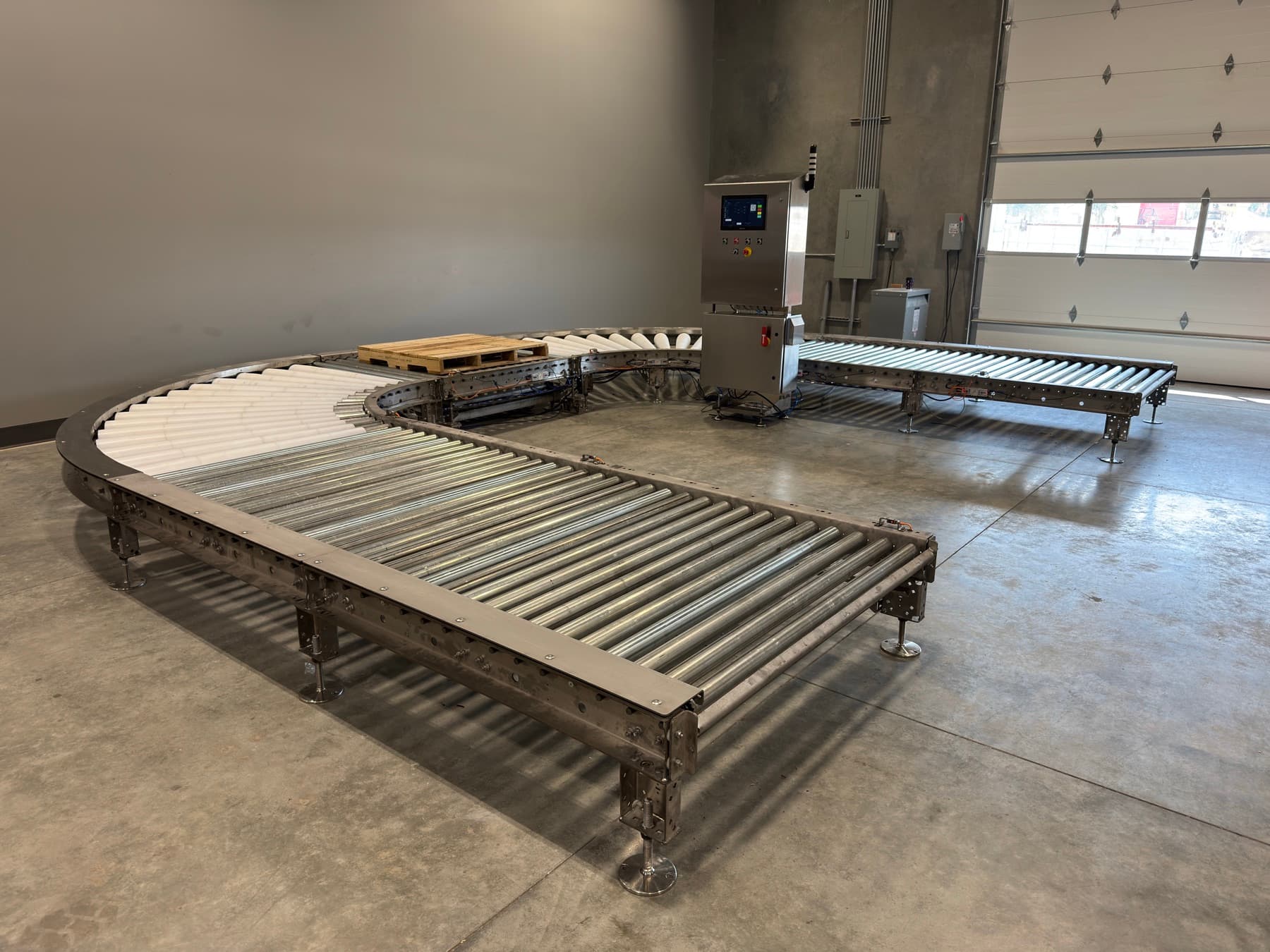 Stainless 24V MDR pallet conveyor loop with tapered-roller curves, a loaded pallet, and a stainless HMI pedestal in the AQS shop