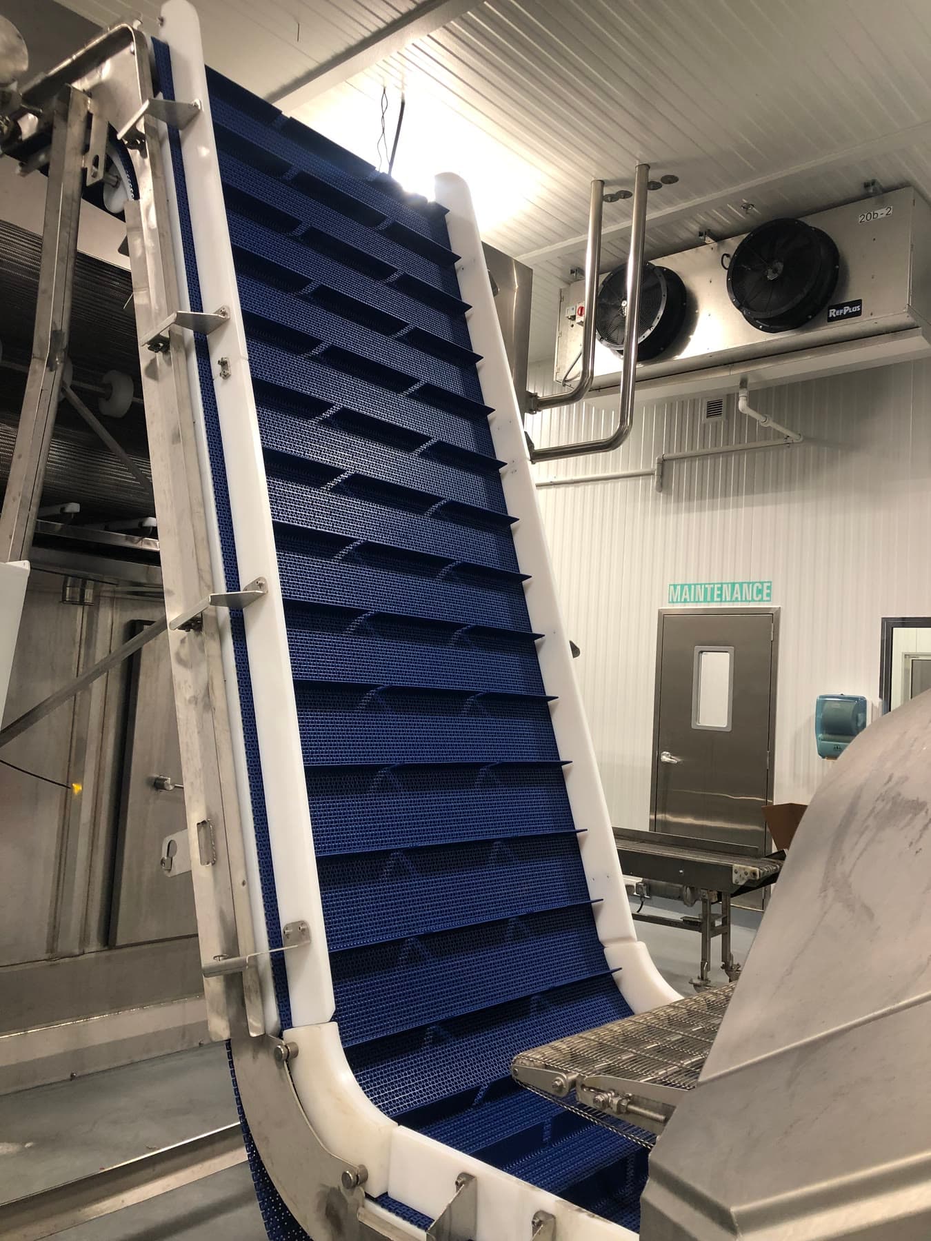 Blue cleated modular belt Z-frame incline conveyor on a stainless frame in a washdown processing room