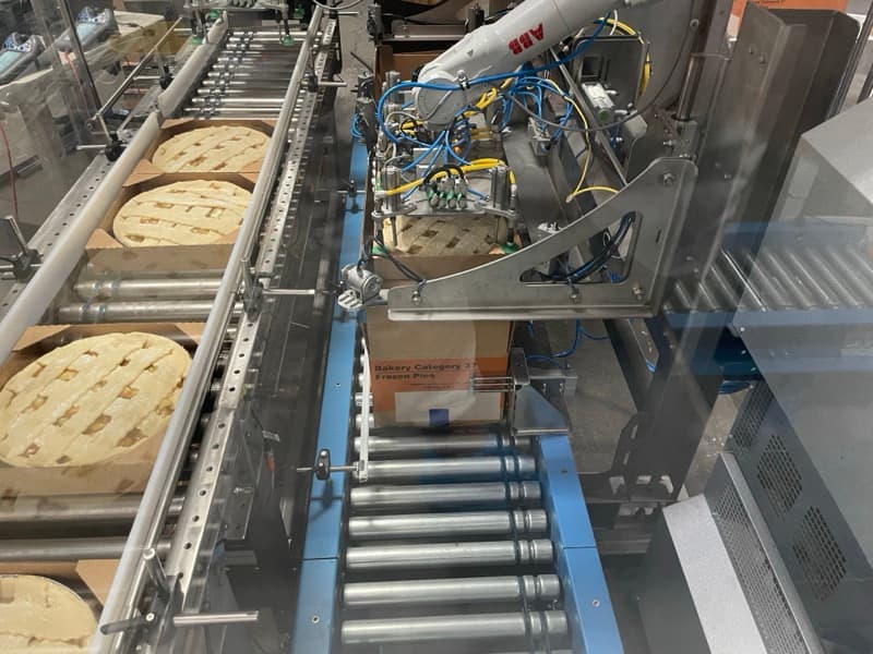 Robotic case packing system handling pies with roller conveyor infeed