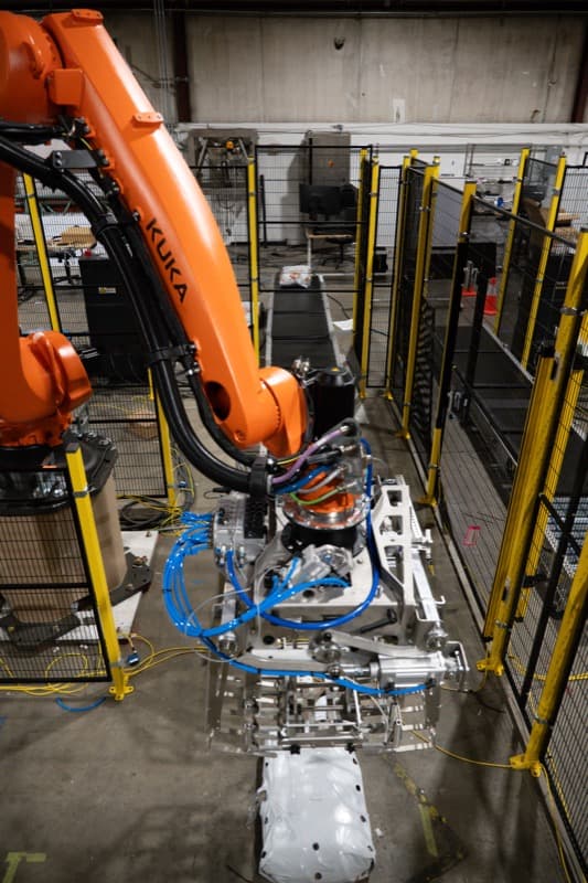 KUKA industrial robot with custom stainless steel end effector in safety cage