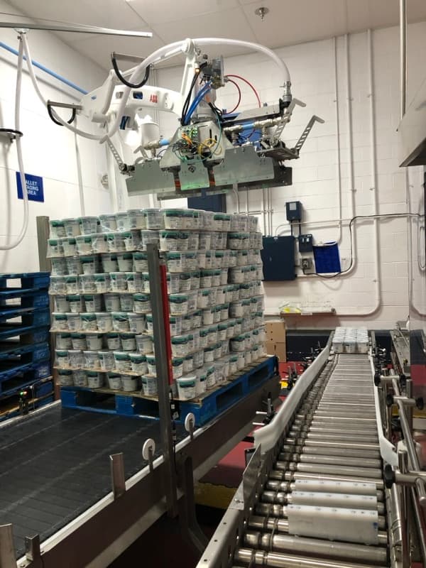 Overhead view of robotic palletizer stacking product onto pallet with roller conveyor infeed