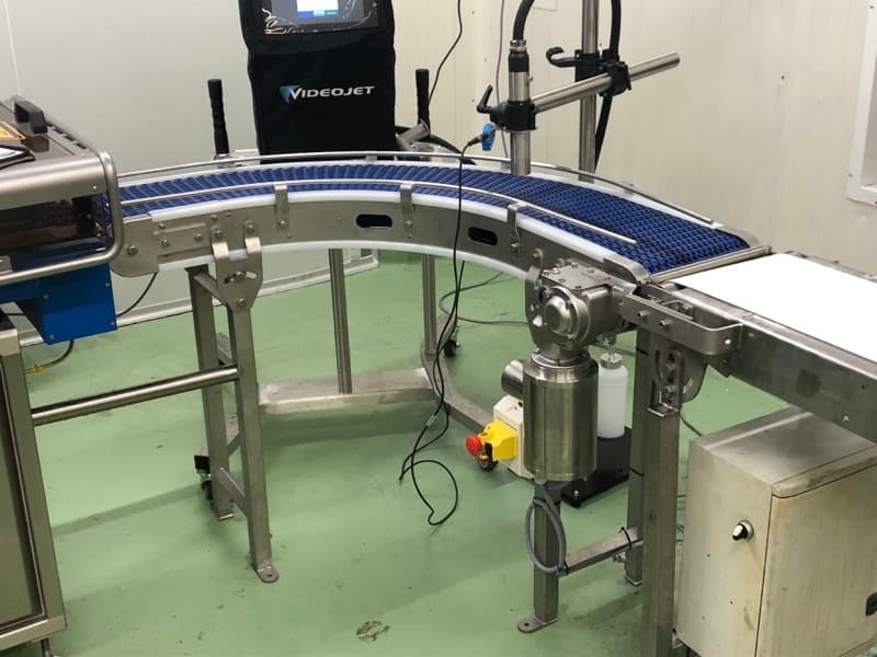 Curved modular belt conveyor on a stainless steel frame rounding a turn in a food plant