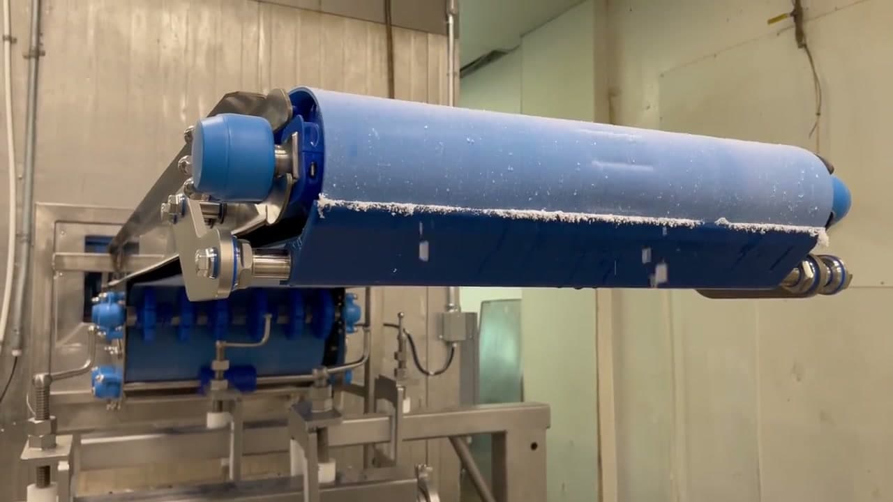 Frosted blue cleated modular belt at the discharge of a freezer conveyor inside a marshmallow production freezer