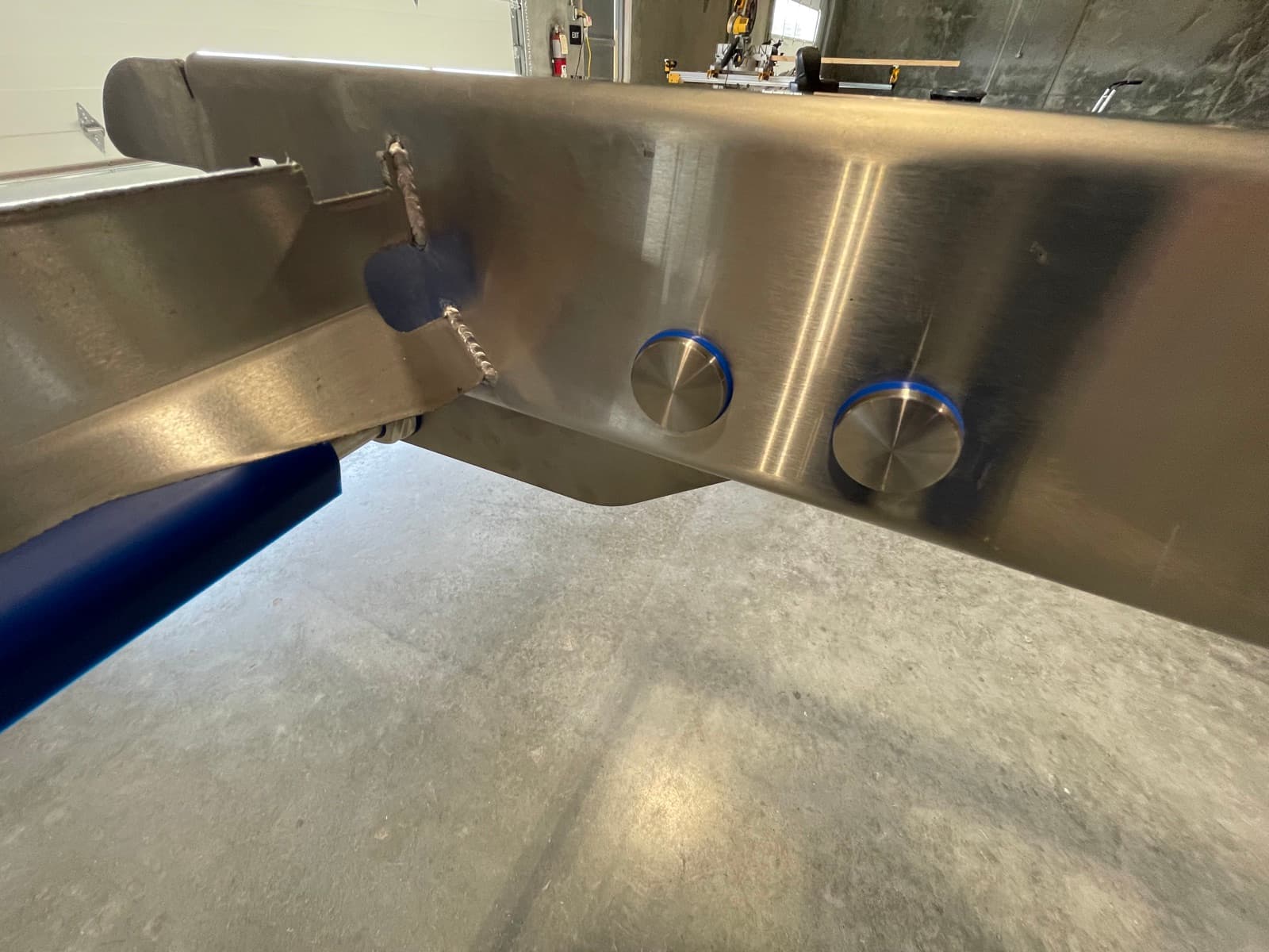 Close-up of a continuous TIG-welded and polished stainless steel conveyor frame joint with blue modular belt